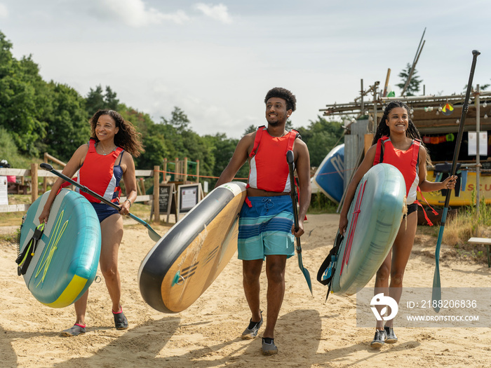 Friends walking with paddleboards on beach