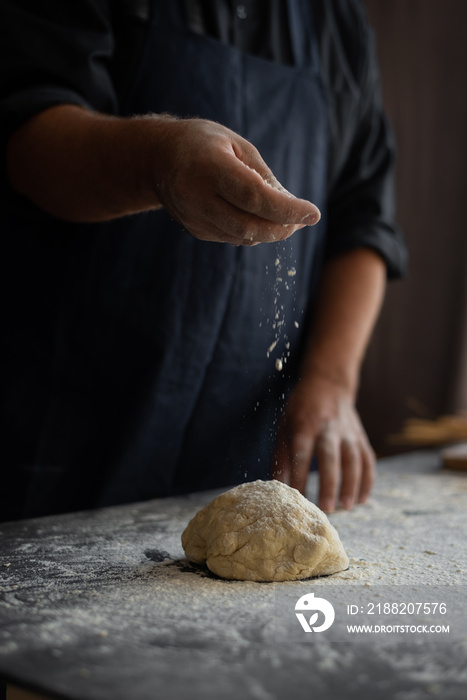 chef cooks cake for pizza, male hands sprinkle raw dough with flour