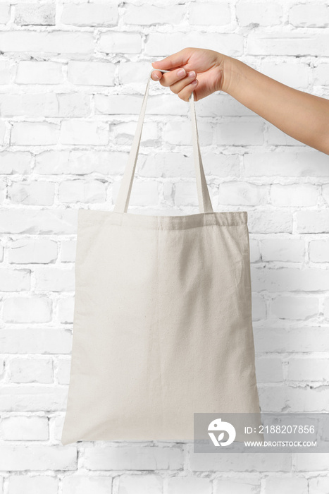 Mockup of female hand holding a blank Tote Canvas Bag on white brick wall background. High resolution.