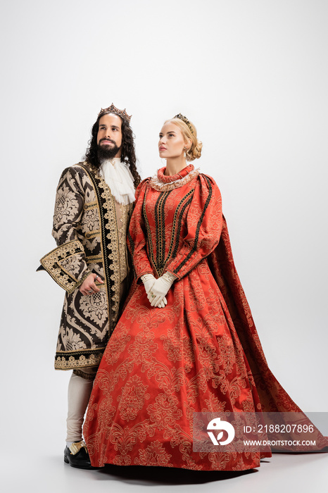 full length of historical interracial husband and wife in crowns and medieval clothing on white