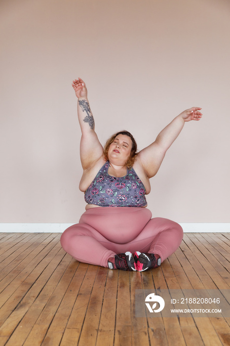 plus size woman sitting on floor arms up