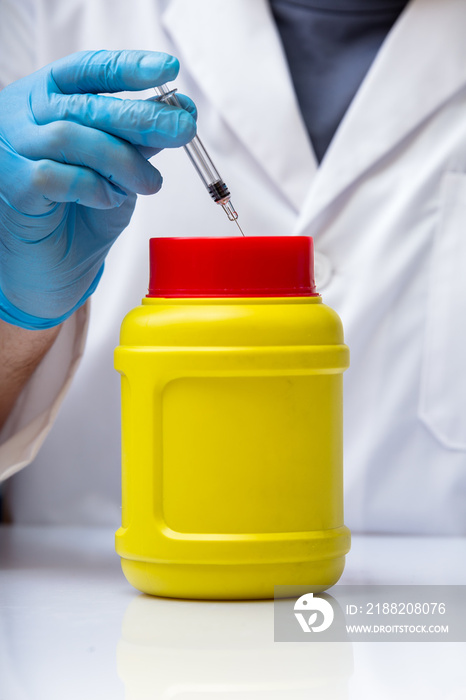 Biohazard waste container / Doctor removing a used syringe in a biohazard waste container