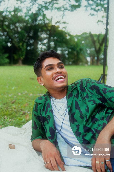 Malaysian Indian men in a group against a cloth backdrop in a park surrounded by trees, talking, laughing and sitting together