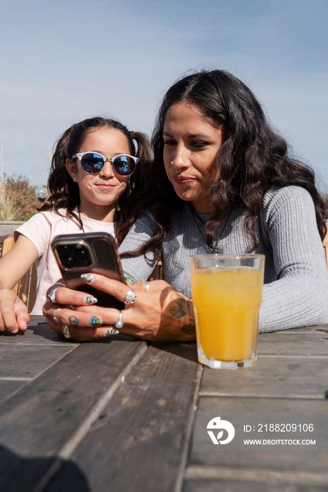 Mother and daughter using smart phone in outdoor restaurant