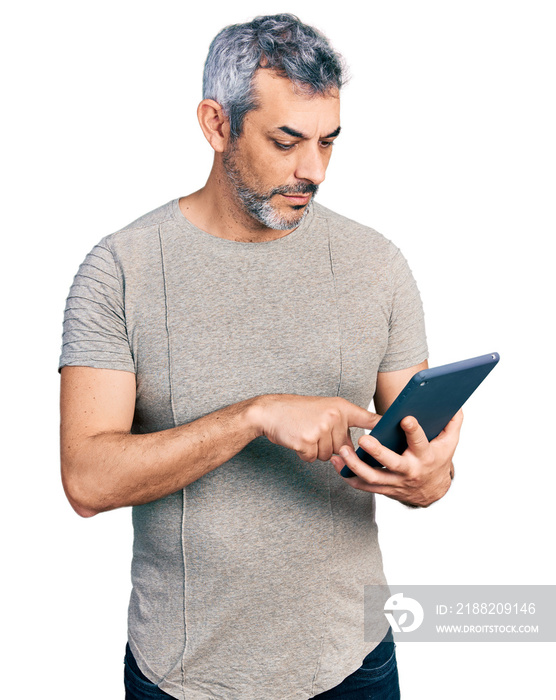 Middle age hispanic with grey hair using touchpad device relaxed with serious expression on face. simple and natural looking at the camera.