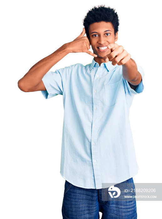 Young african american man wearing casual clothes smiling doing talking on the telephone gesture and pointing to you. call me.