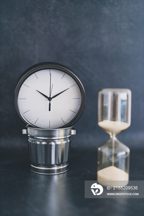 not wasting time, oversize clock with miniature garbage bin and hourglass on business desk