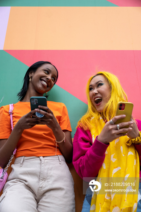 Young female friends using phones outdoors