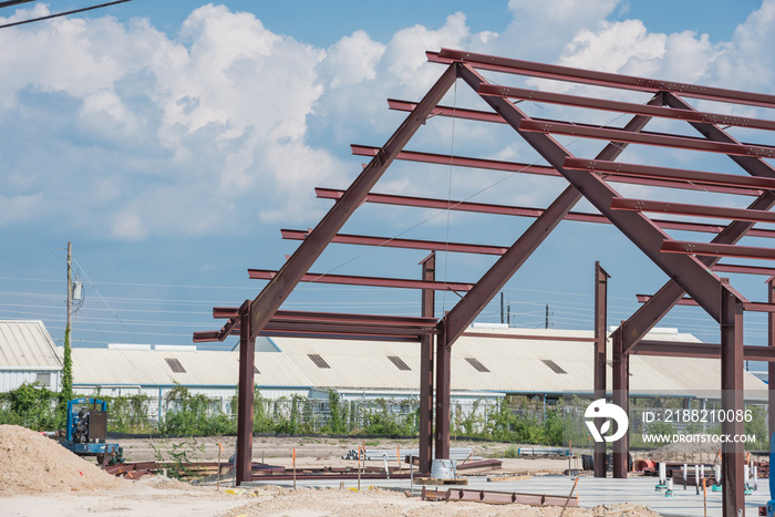 Steel structure of new industrial building under cloud blue sky. New technology structural frame beam of factory in construction. Steel frame manufacturer and pile of sand and gravel in Crosby, TX, US