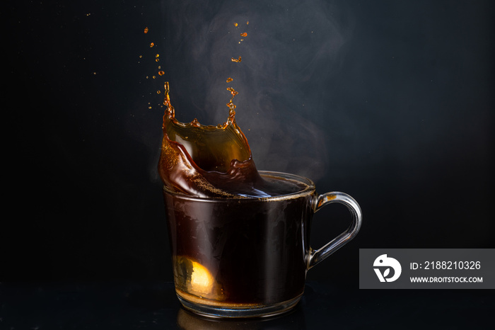 splash and splashes on hot steaming fragrant coffee with steam, smoke in a transparent glass cup on a dark background