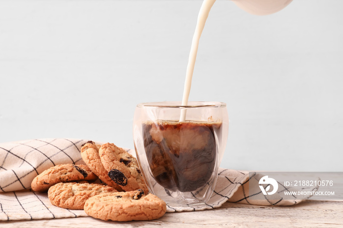 Pouring milk into glass with delicious iced coffee and cookies on table