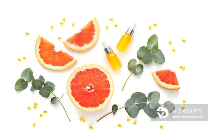 Bottles of essential oil, vitamin A capsules, grapefruit and eucalyptus branches on white background