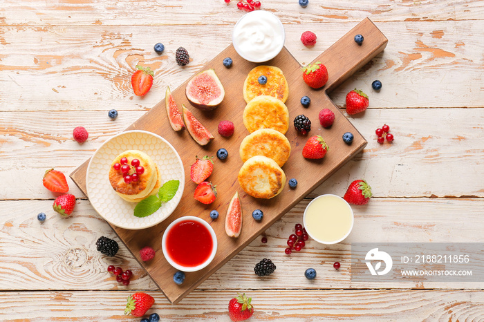 Board with cottage cheese pancakes, berries and jam on light white background