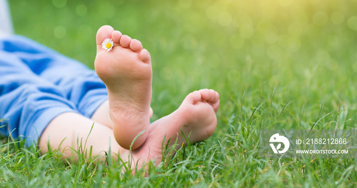 Kid foot on green grass on garden. Barefoot concept, freedom, relax and healthy feet. Panorama banner.