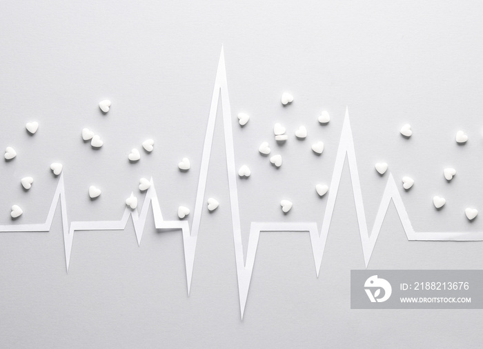 Healthy heart concept. Paper-cut heart rhythm cardiogram with heart-shaped pills on a gray background