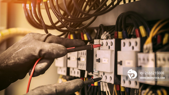 Electrical engineer using digital multi-meter measuring equipment to checking electric current voltage at circuit breaker and cable wiring system in main power distribution board.