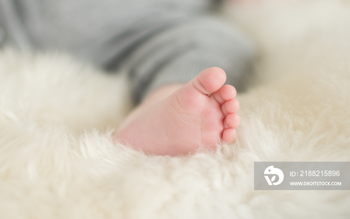 A beautiful soft delicate warm young baby foot photographed with a shallow depth of field. gentle calm colours and feel. baby care and well being. babies feet on a cream fur rug.