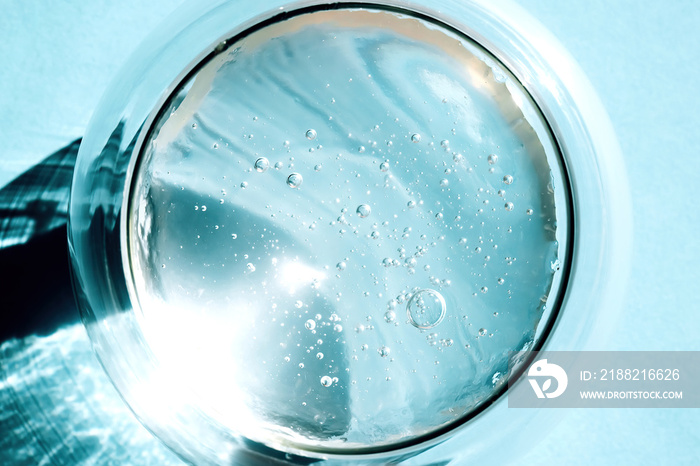 Squeezed cosmetic clear cream-gel texture. Close up photo of transparent aloe vera gel with bubbles in a glass bowl on blue background. Skincare, healthy product.