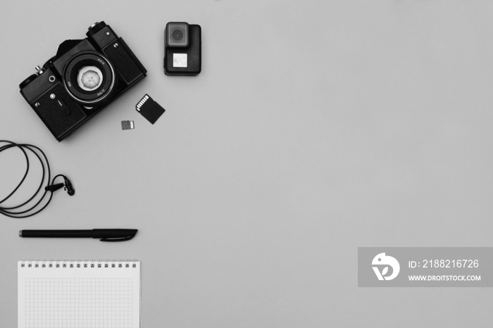 Top view of photojournalist concept with film camera, notepad and action camera on gray background. Office tools.