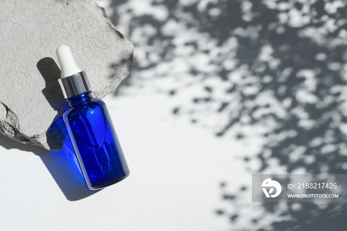 Blue dropper bottles with serum, tonic or essential oil on grey concrete podium. White background with daylight with flowers shadows. Beauty concept for face and body care