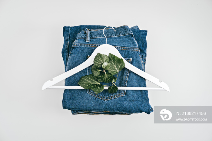 Sustainable fashion, Circular economy, denim eco friendly clothing. Green leaf plant and wooden clothes hanger on blue denim jeans background