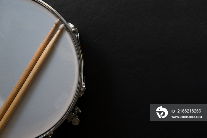 Drum stick and drum on black table background, top view, music concept