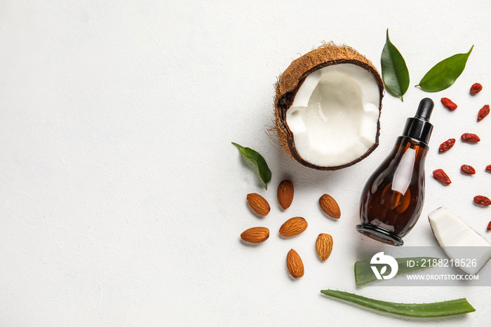 Bottle of natural serum with coconut, plant leaves, goji berries and almond nuts on white background