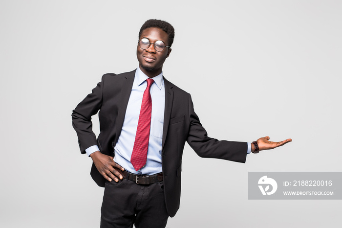 Handsome African American man in a black business suit gesturing as if to demonstrate a product sample on grey