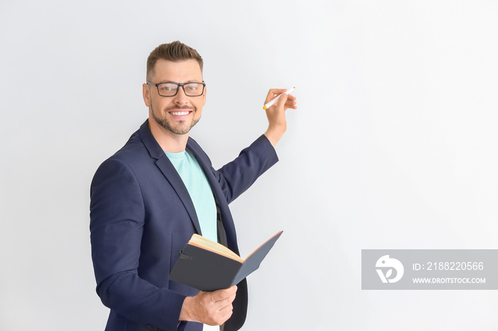 Handsome male teacher writing something on light background