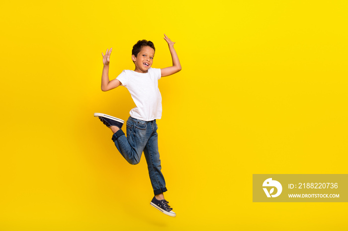 Full size photo of small boy run wear t-shirt jeans sneakers isolated on yellow color background