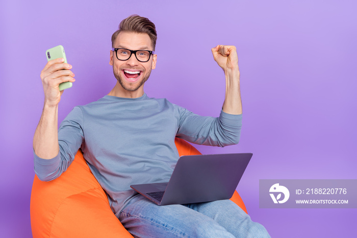 Photo of busy lucky guy dressed grey shirt glasses sitting bean bag reading gadgets empty space isolated purple color background