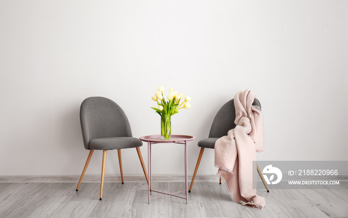 Vase with beautiful flowers on table and comfortable chairs in room