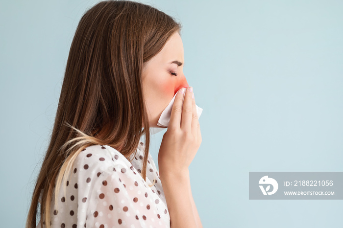 Sneezing young woman on light blue background