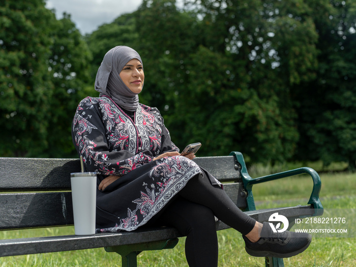 UK,Sutton,Woman in headscarf sitting on bench in park