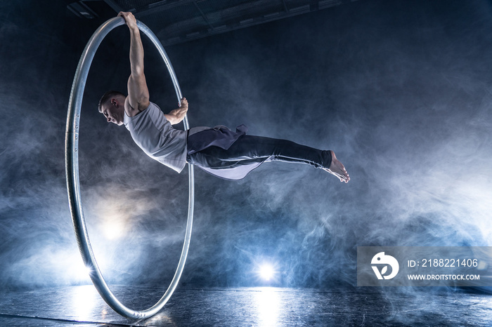 Cyr Wheel circus artist on smoked, dark background performing on stage