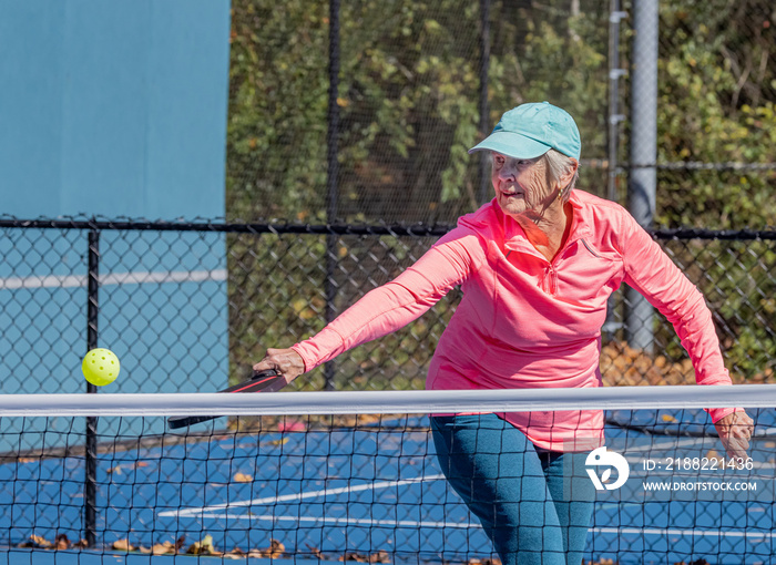 Senior woman strikes a sliced backhand volley during pickleball game in autumn