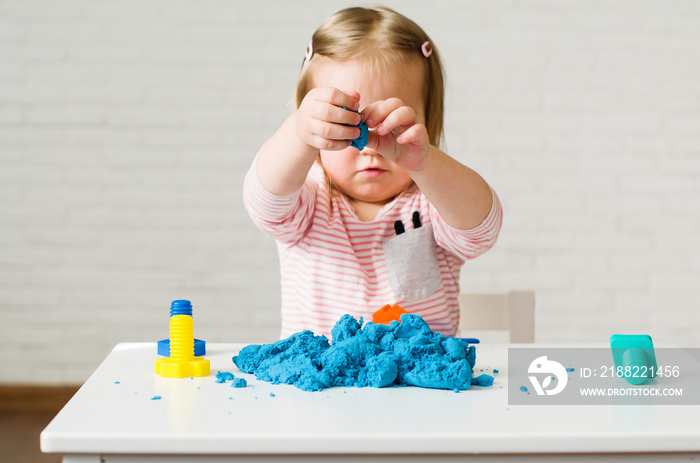 Little girl playing with blue kinetic sand. Educational games with children for fine motor skills. Sand therapy indoors. Concept of sensory and creativity game, therapy hand, development of fine motor
