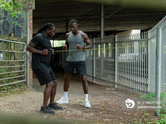 Two men doing strength training with resistance band outdoors