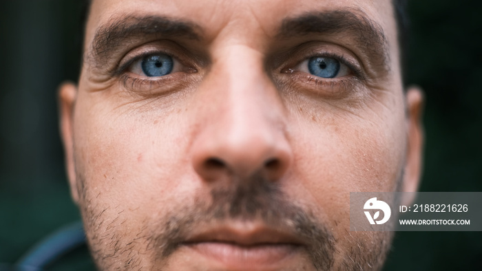 Close-up face of a young man with bright blue eyes looking seriously with curiosity