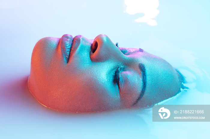 Eyelashes. Beautiful female face in the milk bath with soft glowing in blue-pink neon light. Copyspace for advertising. Modern neoned colors, foam. Beauty, fashion, style, skincare concept. Attractive