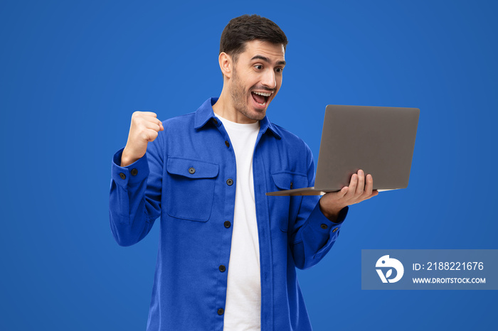 Excited sucessful modern business man holding laptop and raising arm up to celebrate achievement