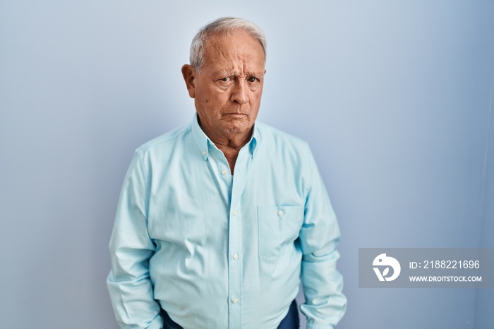 Senior man with grey hair standing over blue background skeptic and nervous, frowning upset because of problem. negative person.