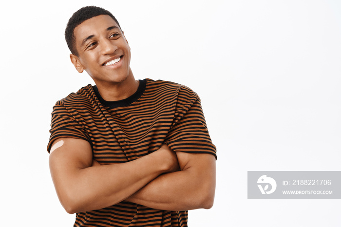 Health and vaccination concept. Smiling healthy african american man, 30 years, has band aid on shoulder after covid vaccine shot, white background