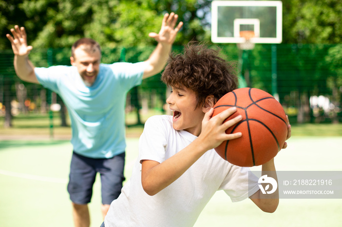 Excited dad playing basketball with his son outdoors