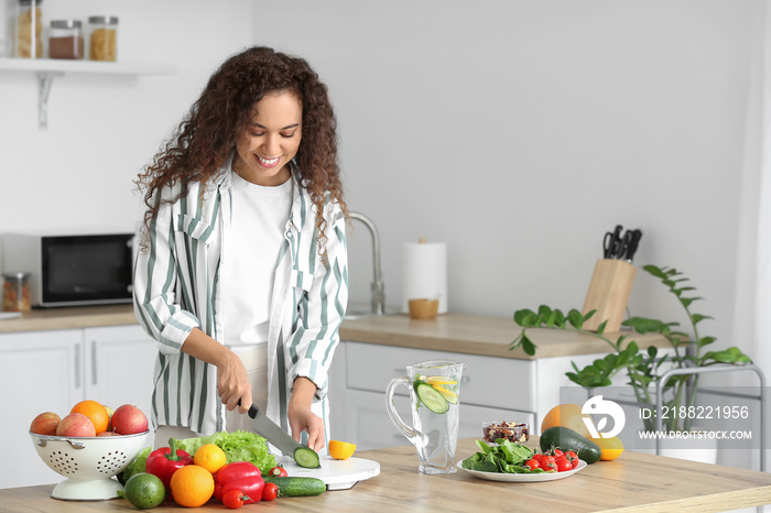 Young African-American woman cutting vegetables in kitchen