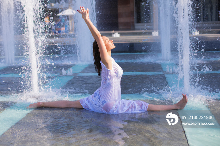 young woman doing monkey yoga pose in city fountain