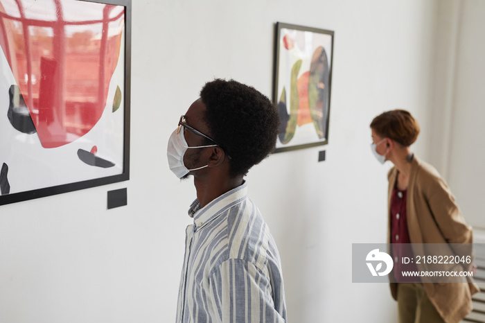 Portrait of two young people looking at paintings while wearing masks at modern art gallery exhibition, copy space