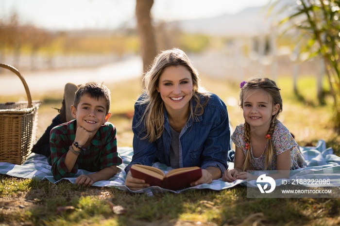 Smiling mother and kids reading novel in park