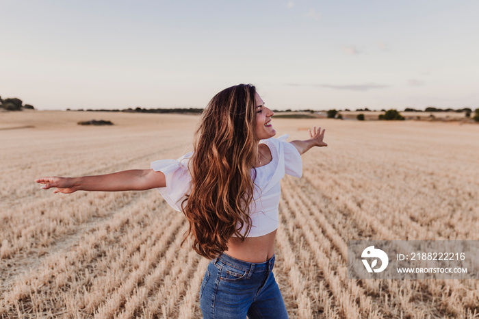 Summer Girl enjoying nature on yellow field. Beautiful young woman dancing Outdoors. Long hair in the wind. Happiness and lifestyle. Back view