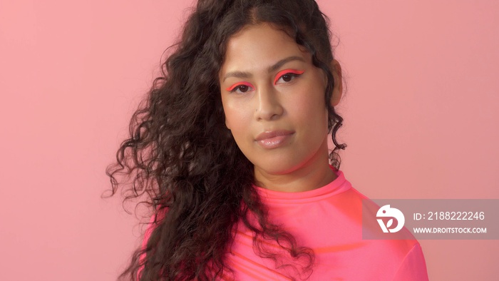 Young plus size mixed race woman with curly hair wears a bright neon makeup and wind round her hair on finger. New beauty concept